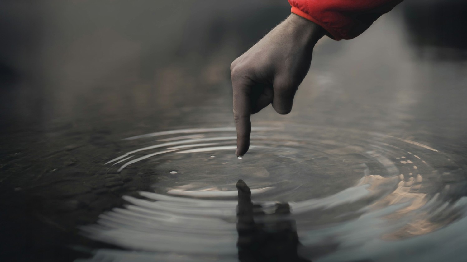 Hands with a finger touching the still surface of a lake