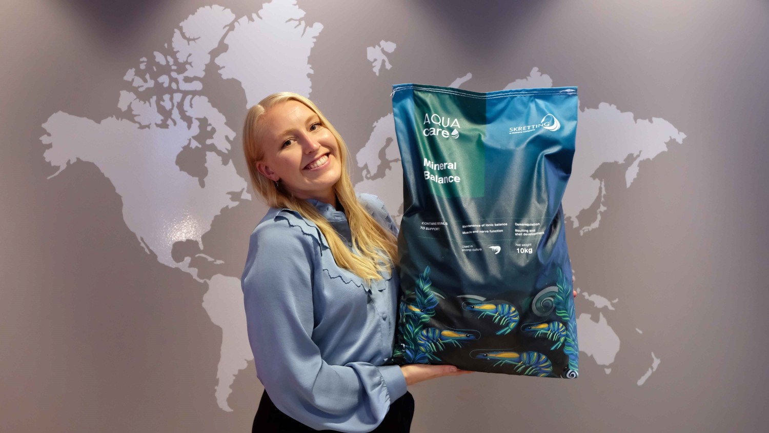 Marita Sirecaag with Mineral Balance feedbag in front of a grey wall map