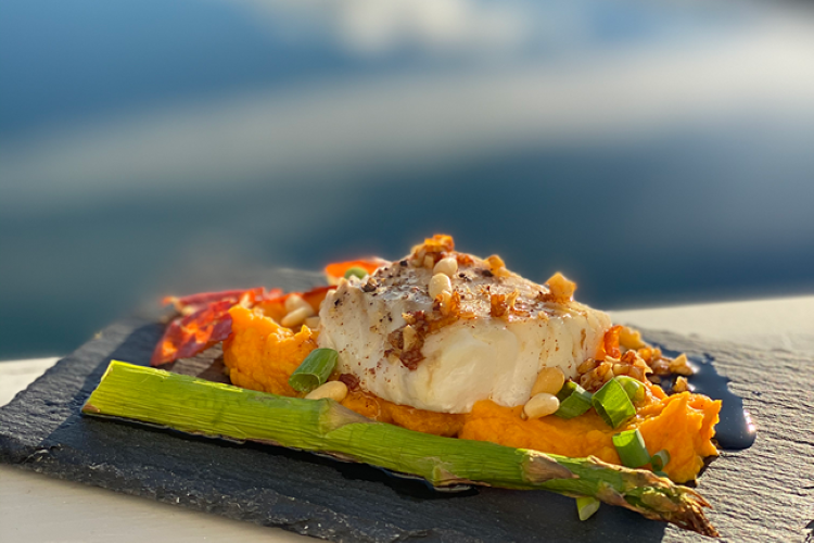 A plated cod dish with vegetables, resting on a rock